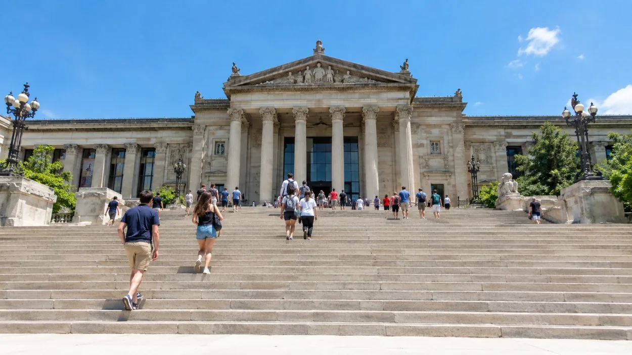 A wide flight of stone museum steps with people climbing on a sunny day