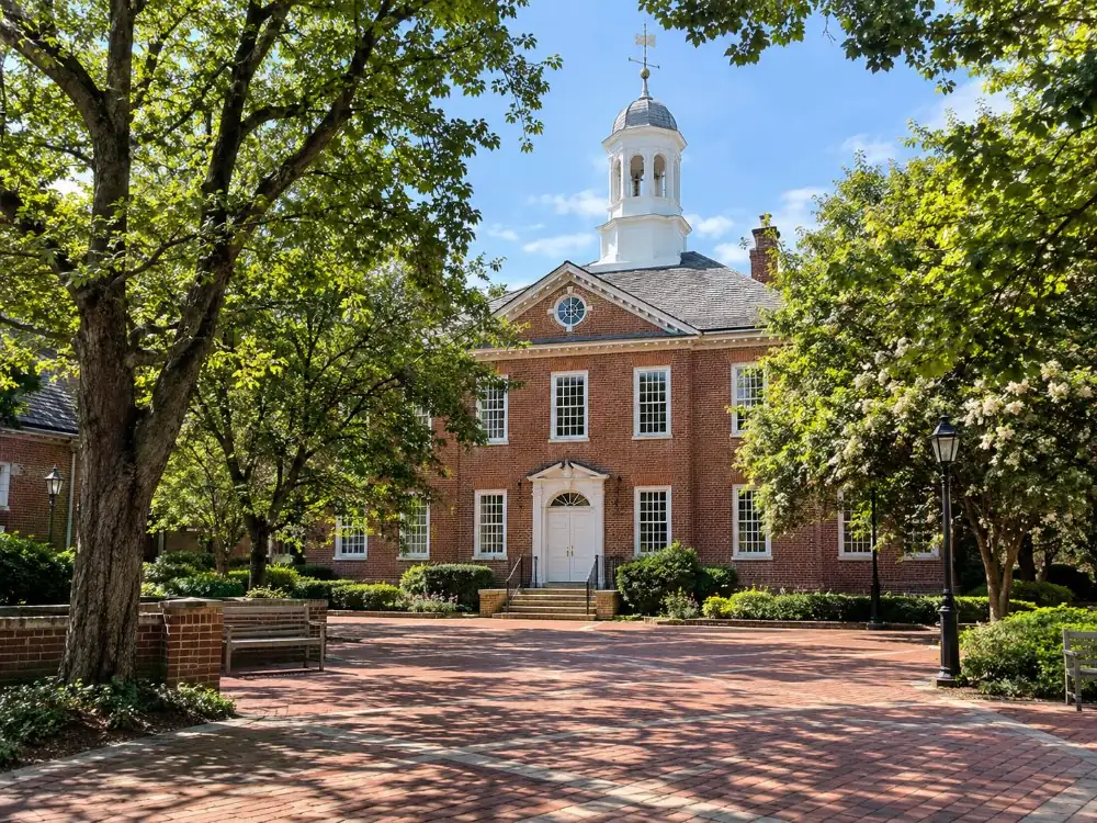 A red-brick colonial hall with a white cupola among trees